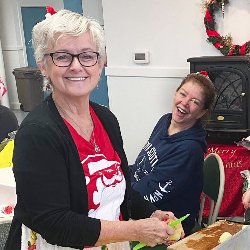Two smiling women preparing food for a community Thanksgiving dinner.